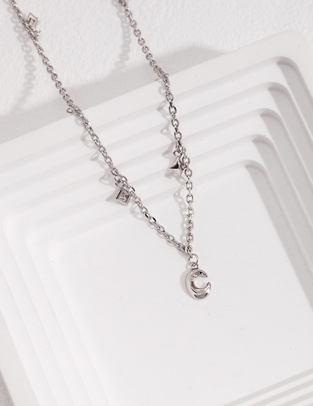 A silver necklace adorned with delicate celestial charms, featuring a moon and stars.