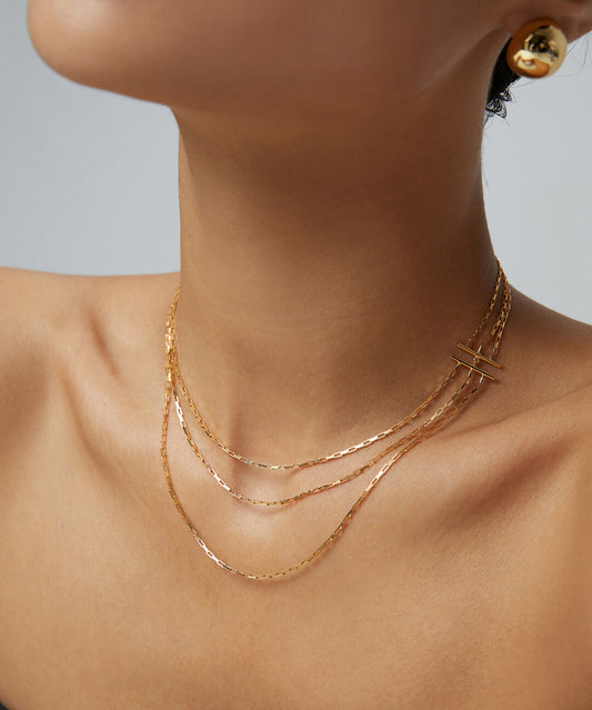 A woman models a triple-layer gold chain necklace, elegantly adorning her neck with the shimmering accessory.