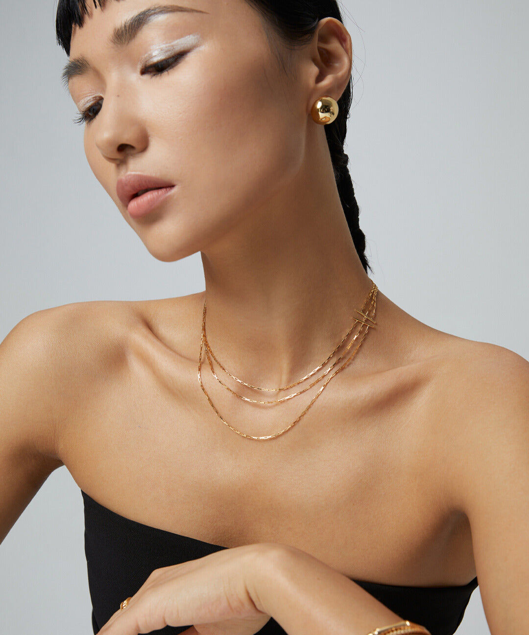 A woman showcasing her exquisite style with a triple-strand gold chain necklace and earrings.