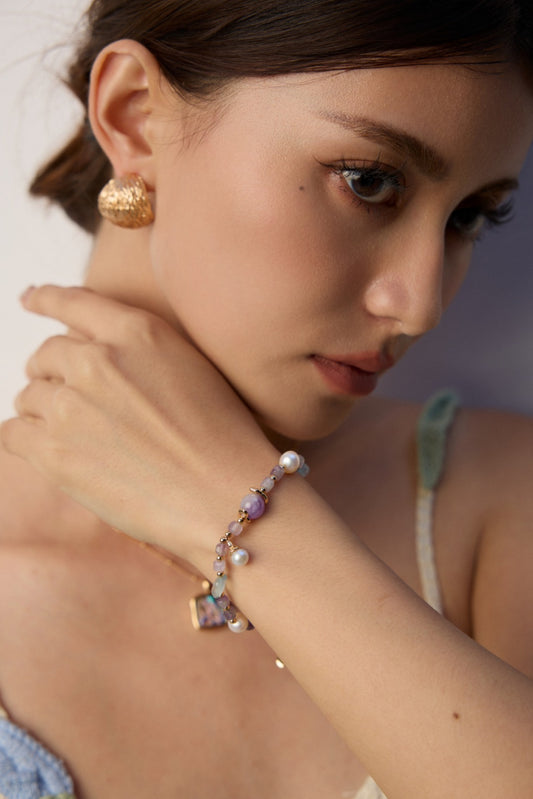 Close-up of a woman's wrist featuring a gold chain bracelet with amethyst and icy aquamarine stones.