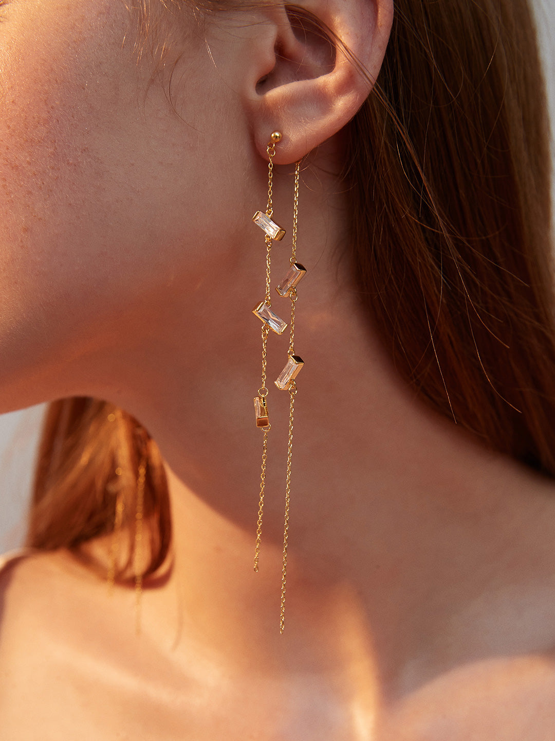 Close up shot of model wearing an elegant crystal-adorned gold chain earring, ideal for adding a touch of glamour to any outfit.