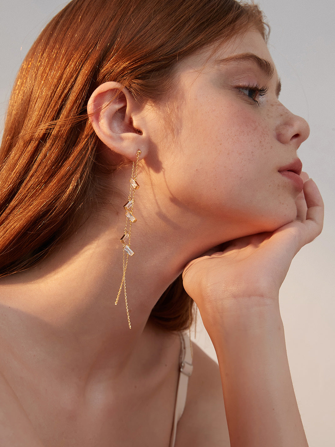 Woman wearing a gold cubic zirconia dangling earring with long chain.