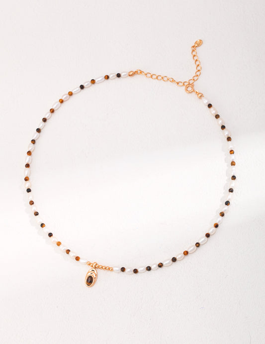 Stylish gold and black necklace adorned with tiger's eye and freshwater pearl beads, accented by a small charm.