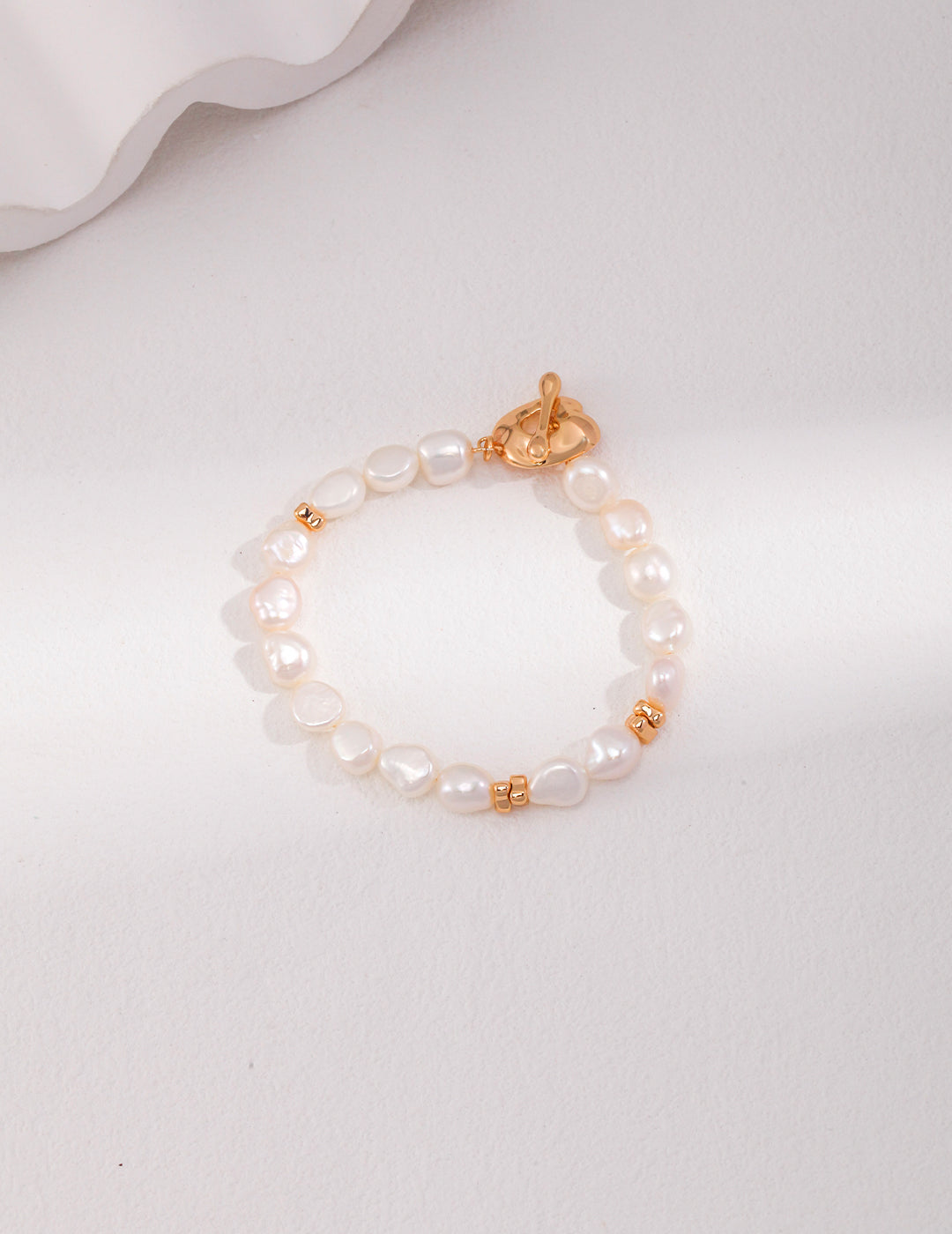 Stylish gold bracelet with white pearls on white table