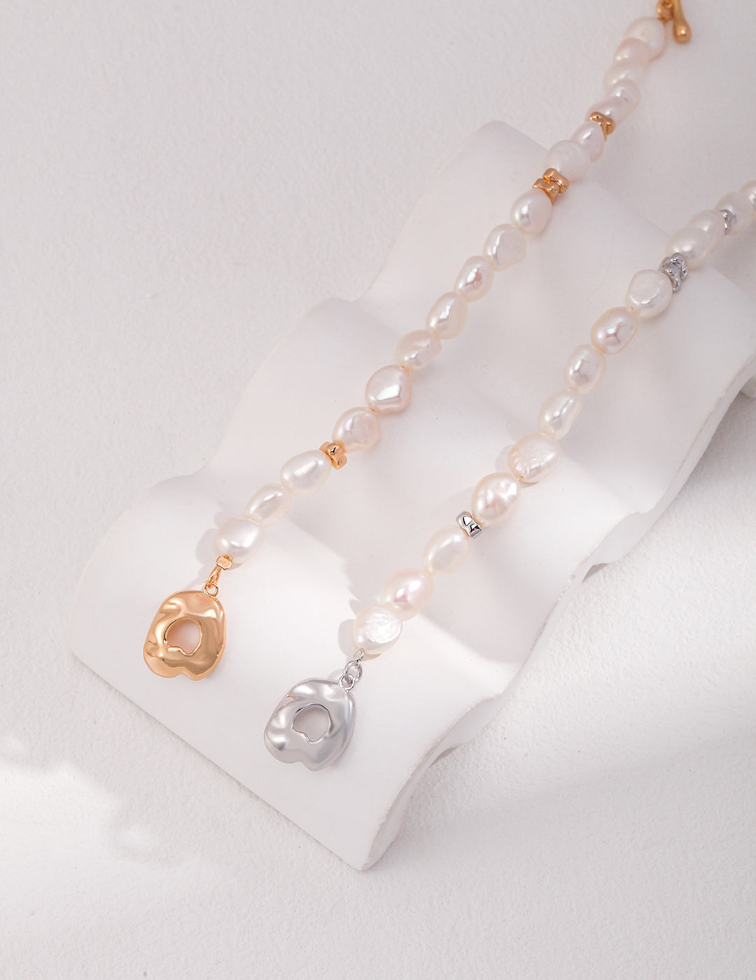 Two pearl necklaces with gold and silver charms: one silver, one gold.