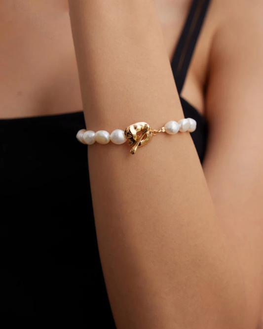 Close-up of a woman’s wrist featuring a baroque pearl bracelet with gold leaves and a gold band.