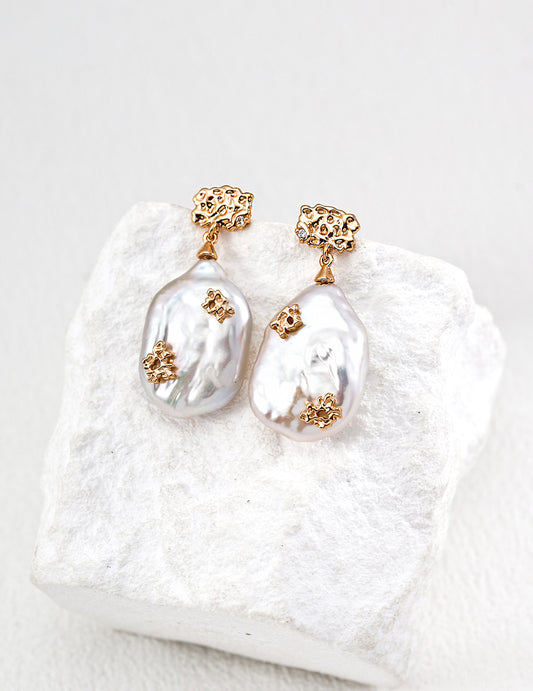 A pair of Vanessa Earrings with pearls gold accents on a textured white surface