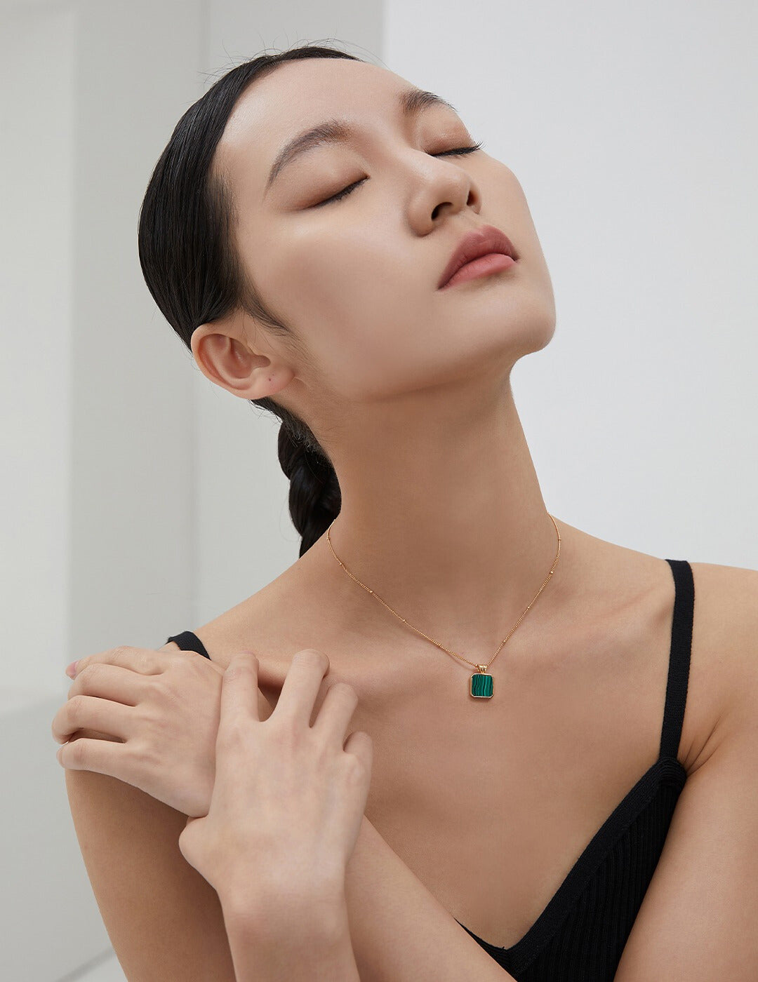 Fashionable lady showcasing a black top and a gold plated necklace with a luxurious malachite pendant.