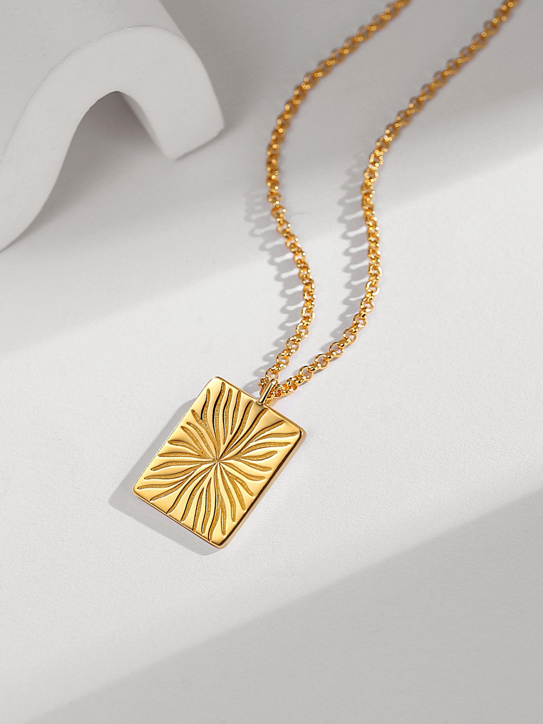 Gold plated square necklace with gold vein design on white surface.