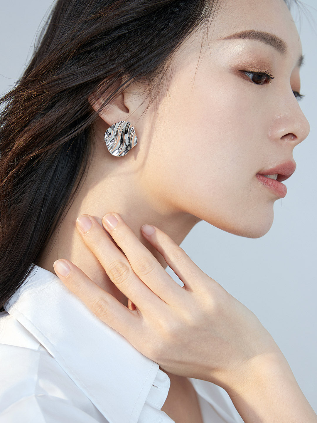 A woman in a white shirt wearing silver textured wave earrings.