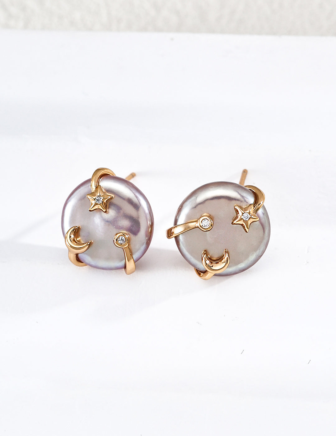 A detailed close-up studio photograph showcasing the gold vermeil Vesper Studs, featuring a coin freshwater pearl cradled by celestial star and crescent moon motifs with accent gems.