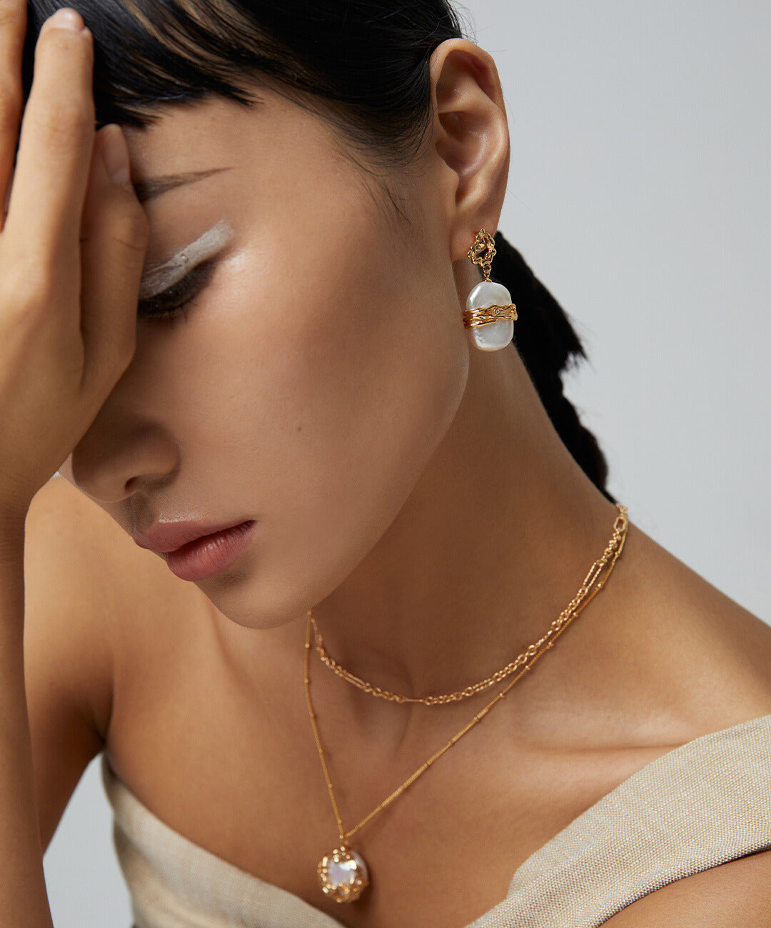 Stylish woman with hand on head, wearing gold necklace and pearls.