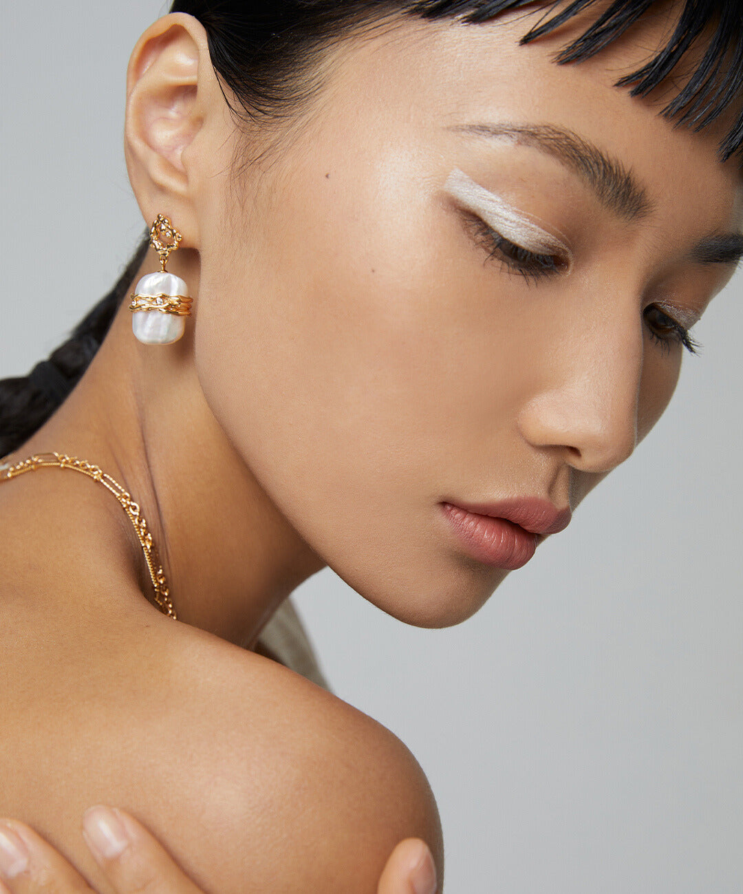 Stylish model wearing gold earrings, highlighting lustrous freshwater pearls.