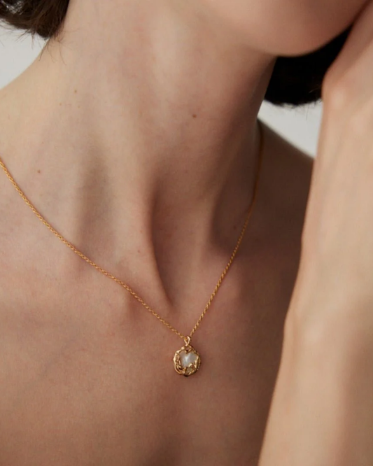 A woman wears a stylish contemporary gold necklace with a pearl, emphasizing modern elegance and fashion.