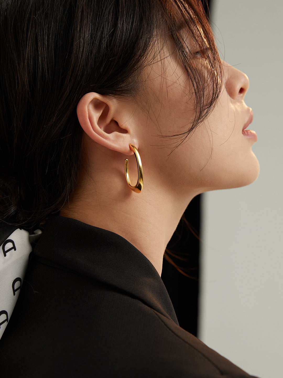 Woman in black blazer with gold hoop earrings, model showcasing stylish accessories.