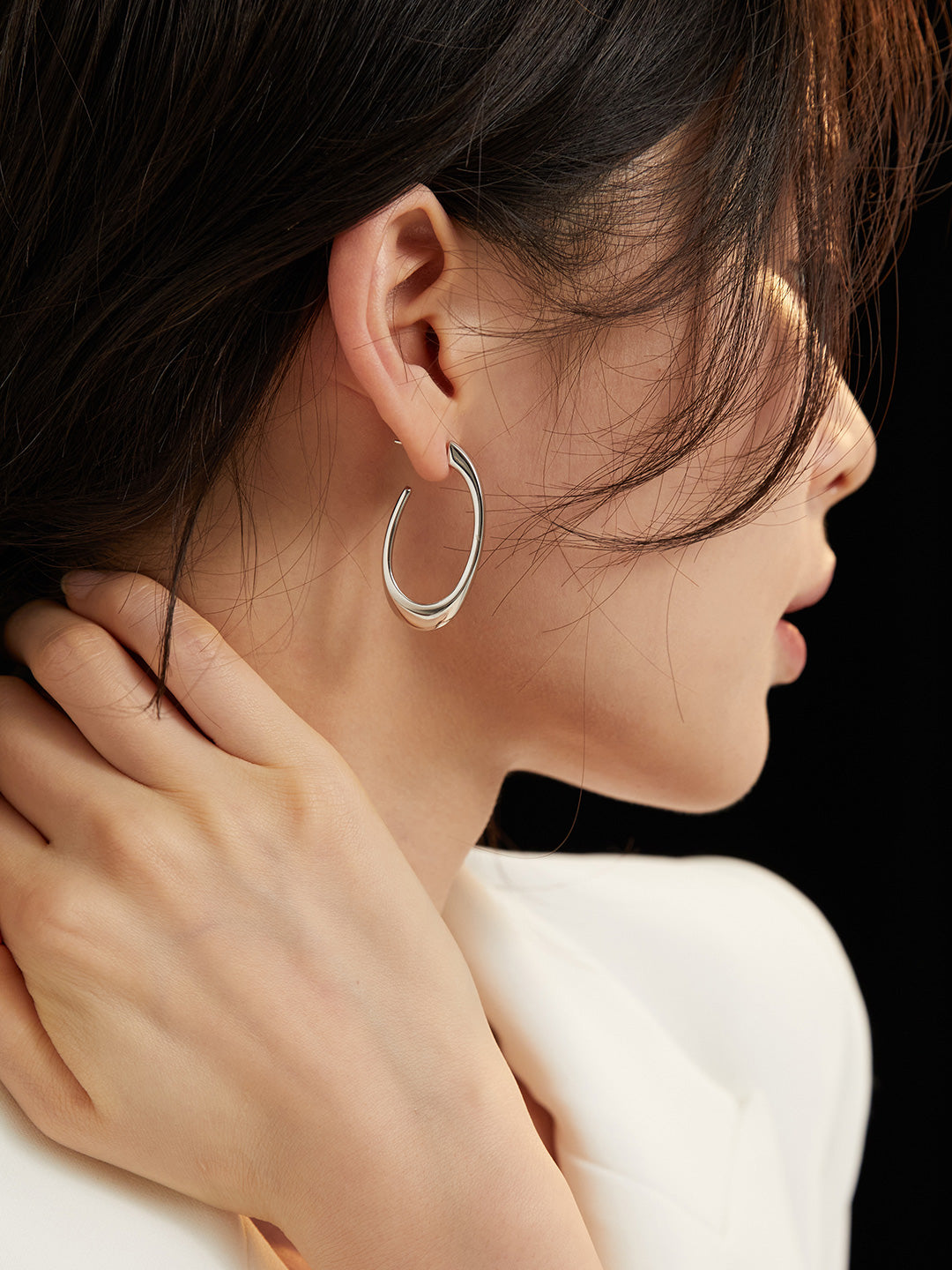 A model wearing a white blouse and silver hoop earrings, looking elegant and stylish.