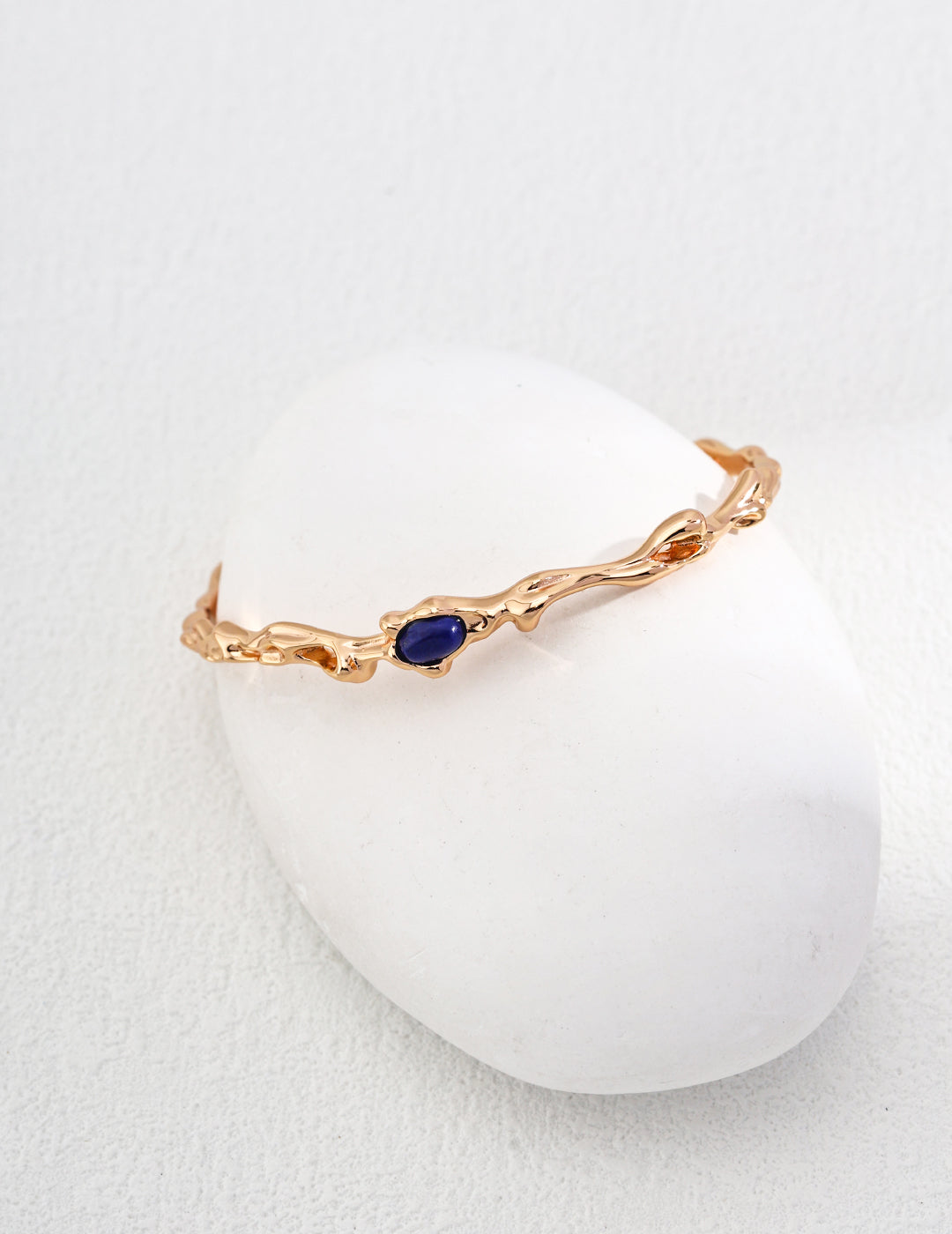 A stunning gold bracelet featuring blue lapis lazuli placed atop a smooth white egg.