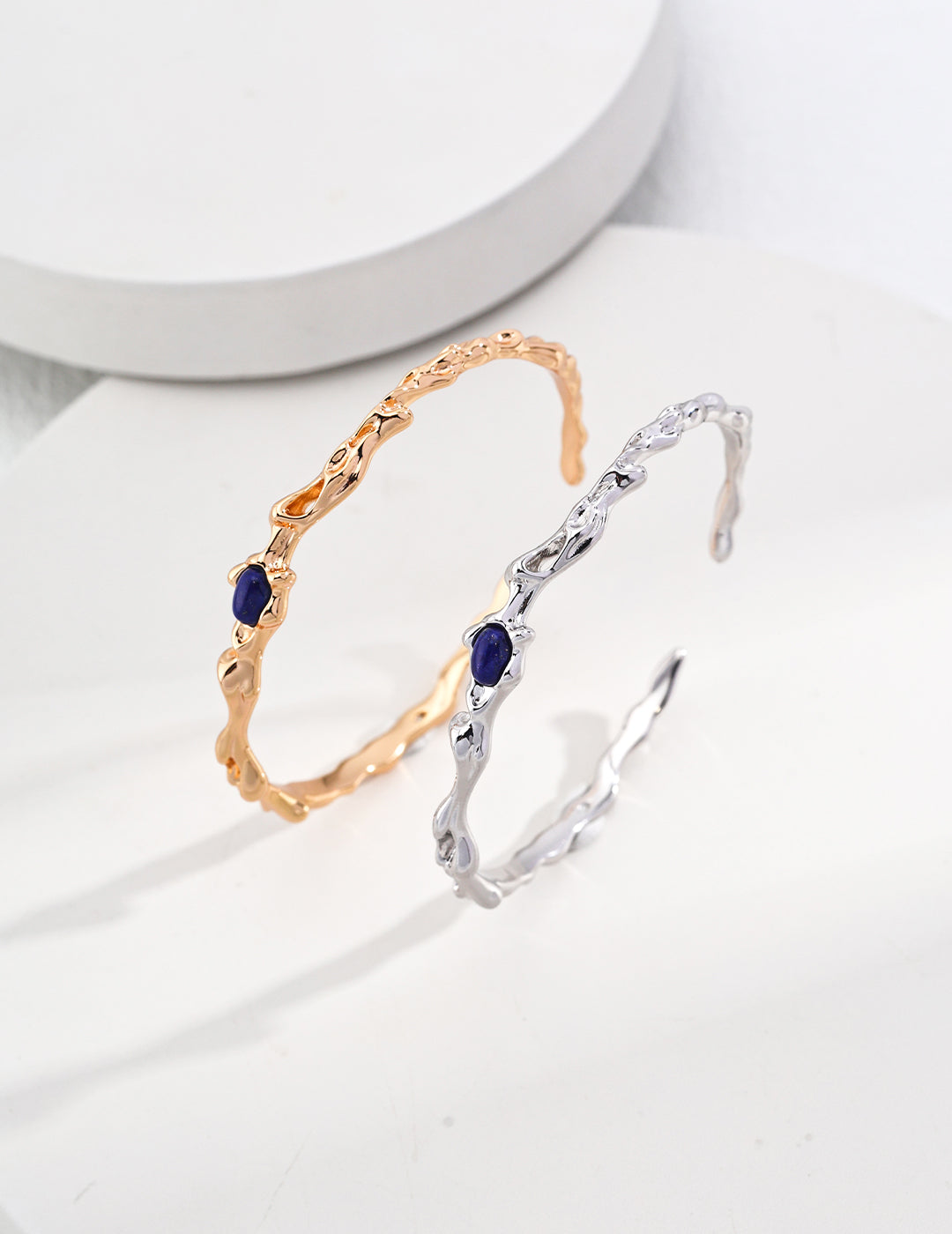 A silver bangle and a gold bangle, both embellished with vibrant blue stones, highlighting their unique beauty.