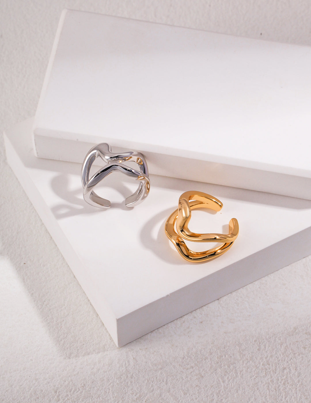 Two double band rings, one gold and one silver, placed on top of a white box.