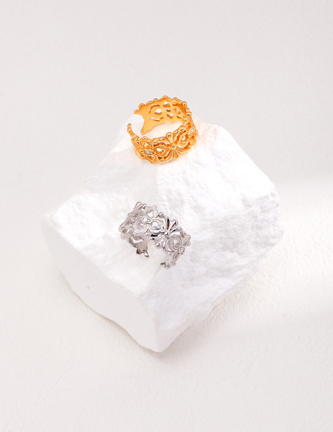 Two silver and gold hollow rings with cubic zirconia sitting on a white rock.