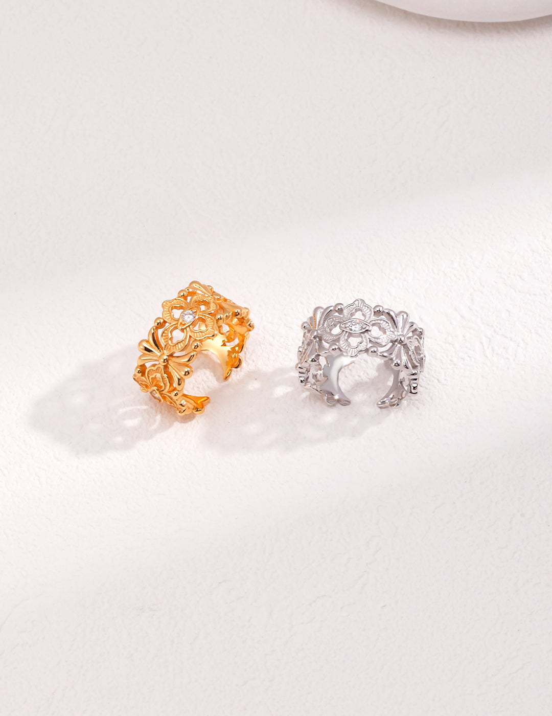 A pair of stunning gold and silver rings featuring intricate flower patterns, embellished with cubic zirconia.