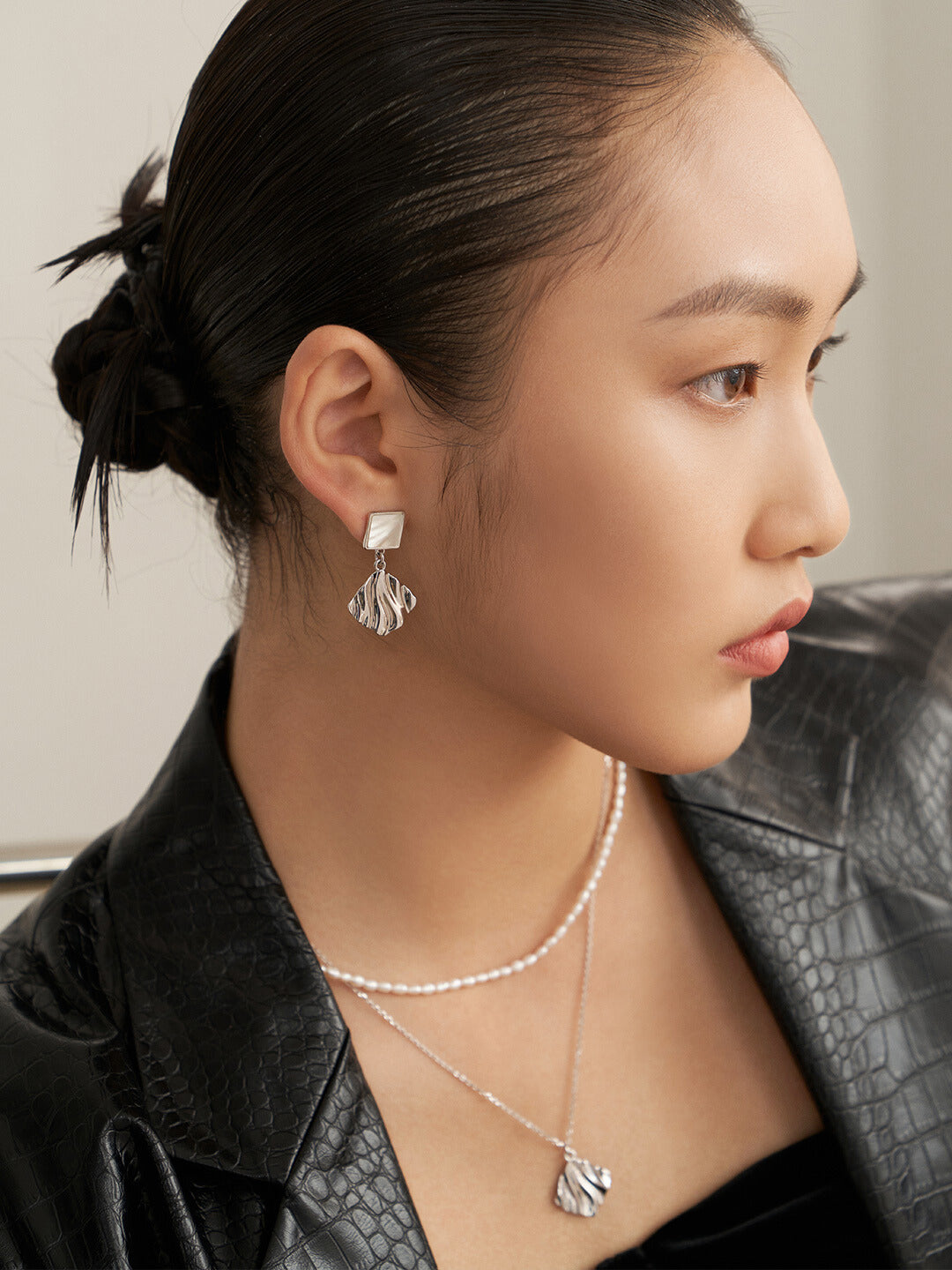 A stylish woman in a black leather jacket and necklace. She also wears silver, nacre, and wavy design earrings.