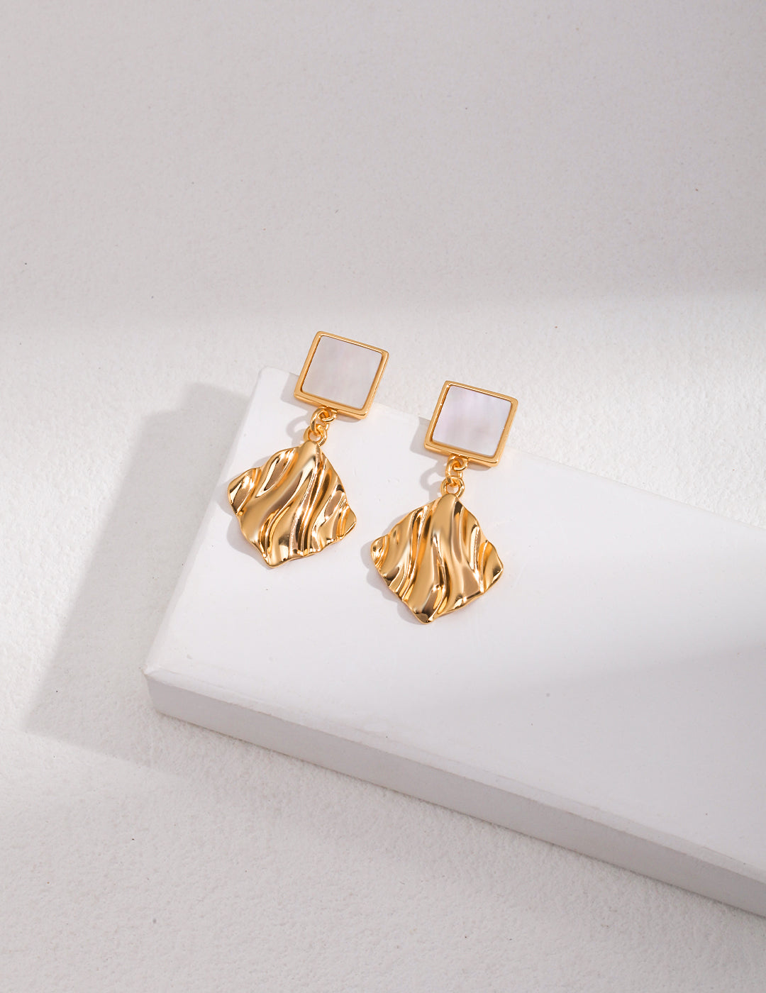 Stylish gold tone earrings featuring a wavy design, resting on a white surface.