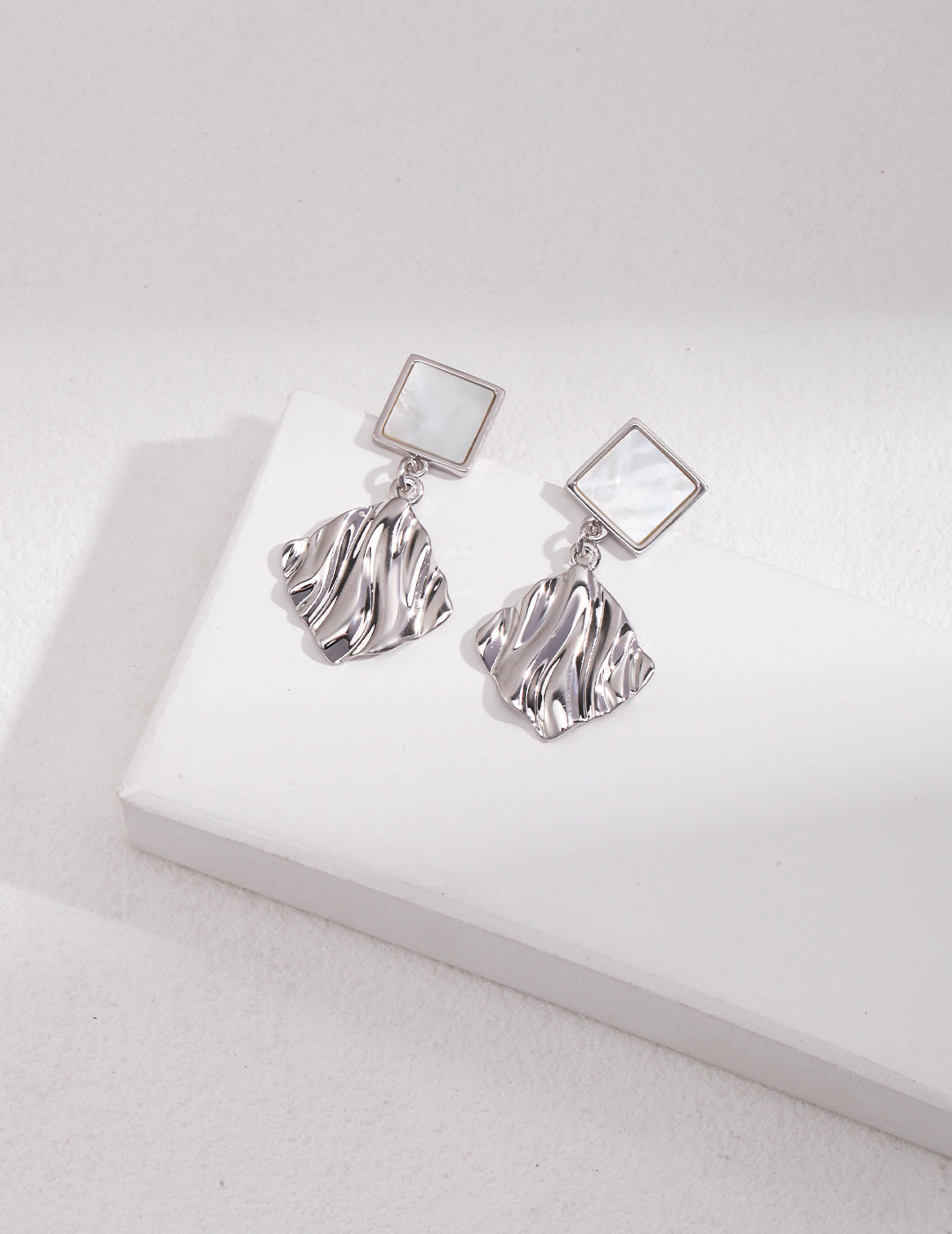 Silver nacre earrings with a wavy design resting on a white surface.