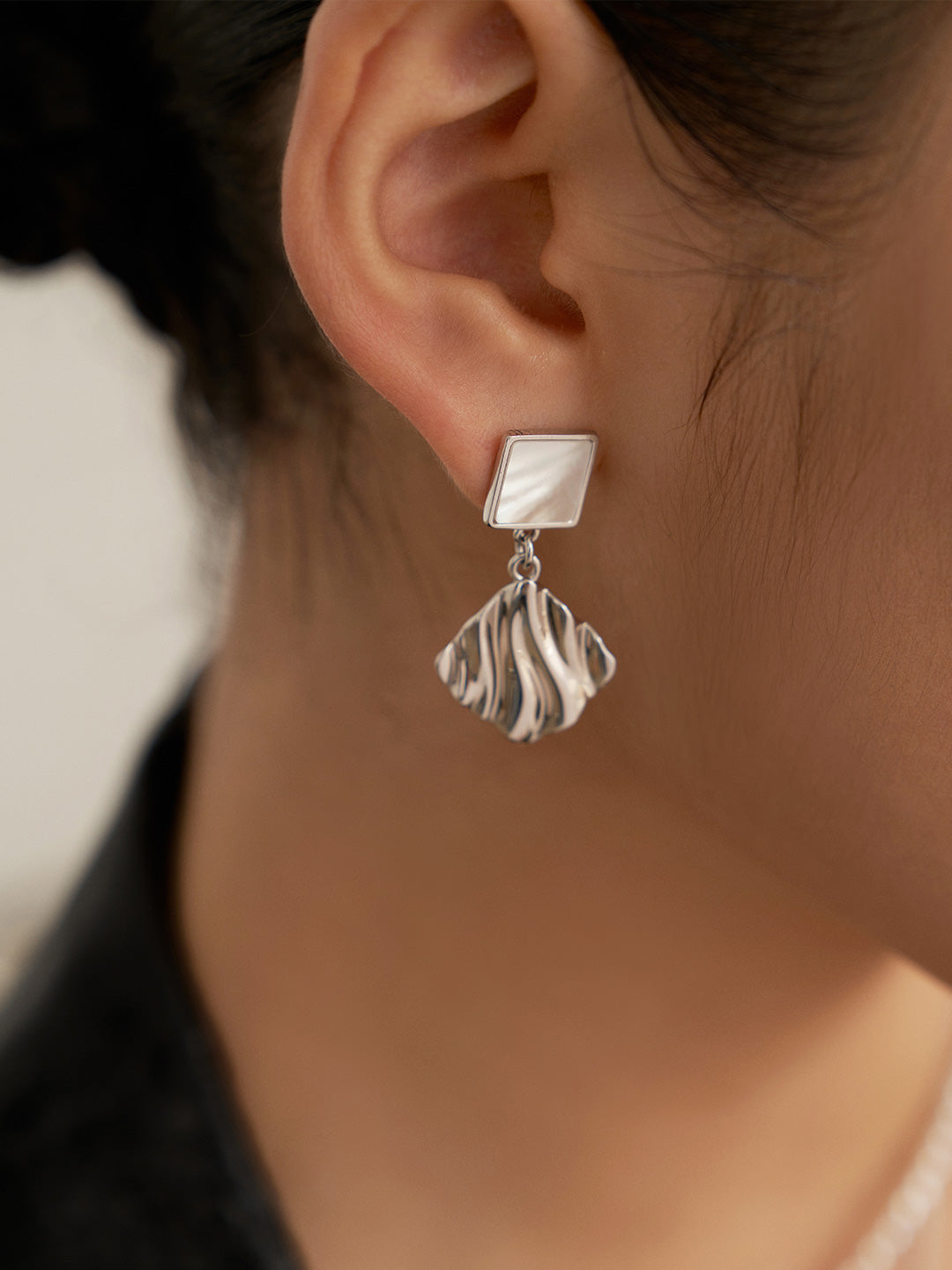 Stylish silver earrings featuring a wavy design, worn by a model, exude elegance and charm.