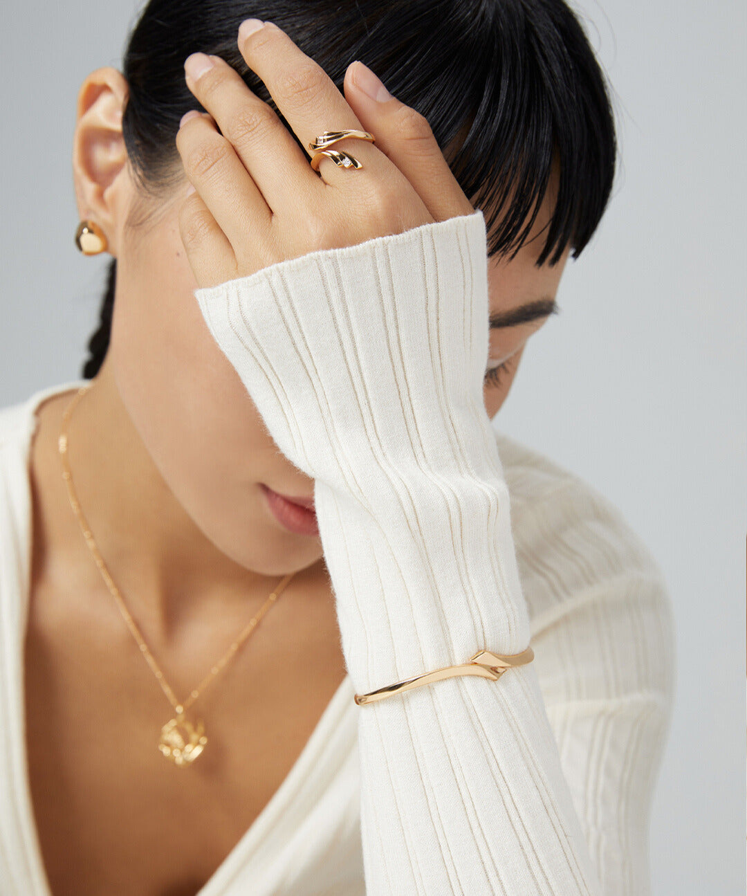 Woman in white sweater with gold jewelry, including a gold bangle.