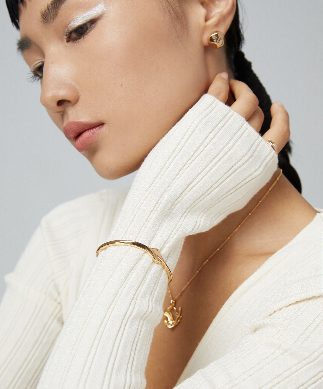 A model wearing a white sweater and a gold bracelet, showcasing elegance and style.