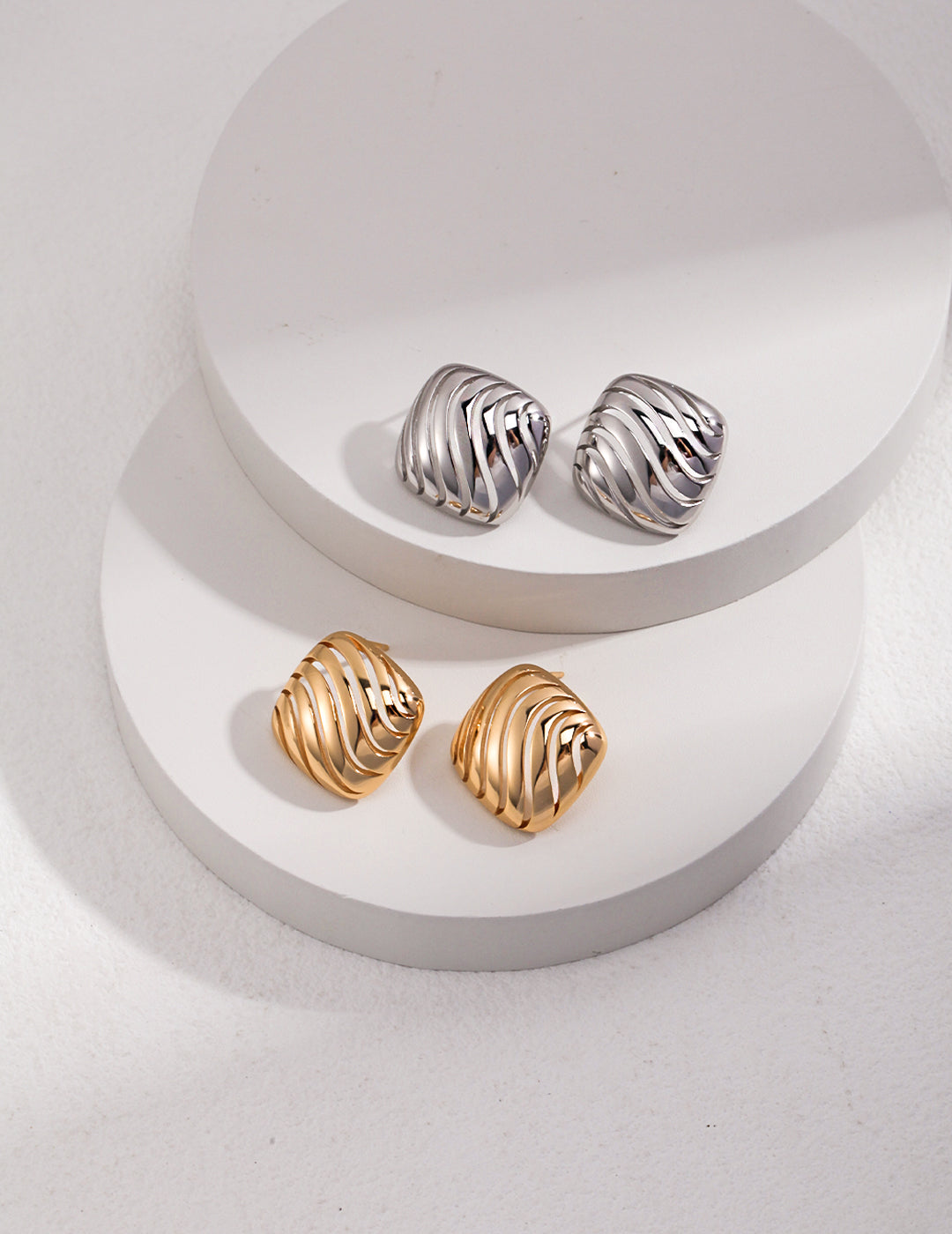 Two pairs of hollow striped earrings, one gold and one silver, displayed on a white surface.