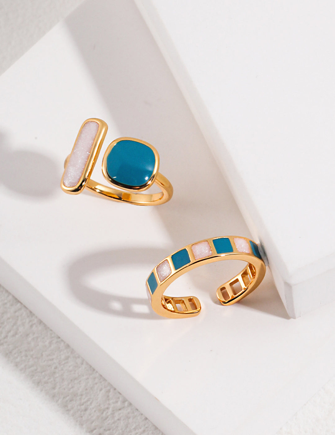 Pair of gold and turquoise rings resting on a white tabletop.